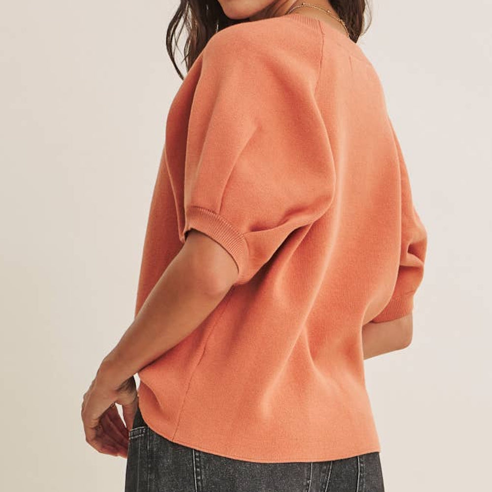 Back view of model wearing a burnt orange short-sleeve knit sweater with puff sleeves and dark jeans.
