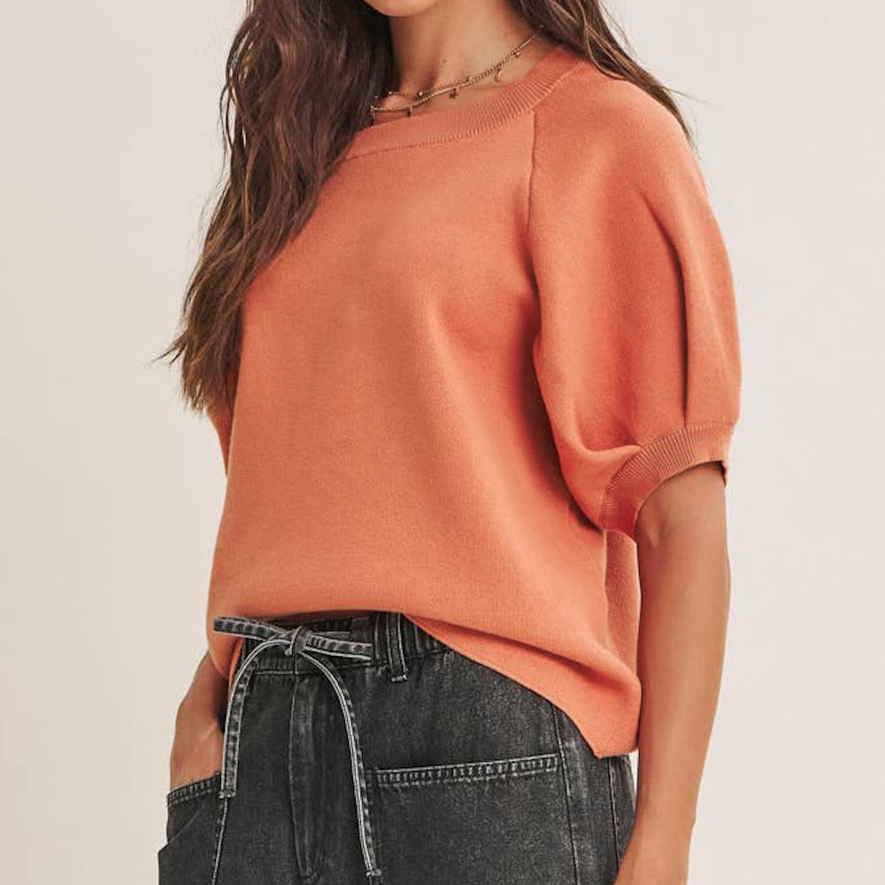 Burnt orange short-sleeve knit sweater with puff sleeves paired with dark gray tie-waist jeans.