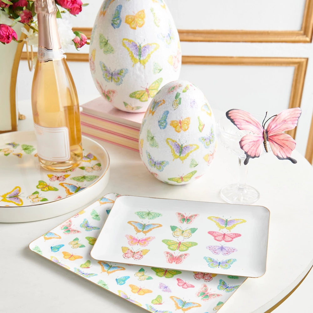 A table with a white tablecloth, featuring a pink glass vase and a decorative butterfly plate.