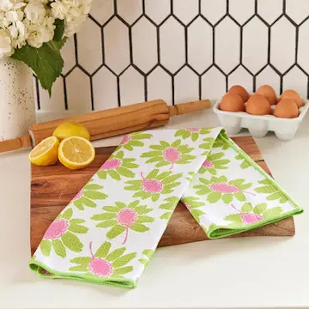 Pink and lime green floral patterned tea towel on a wooden cutting board with lemons, a rolling pin, and eggs nearby.