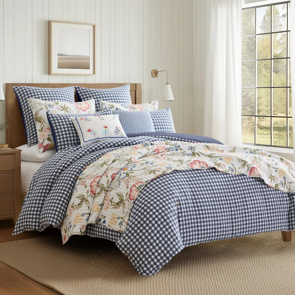 Styled bed featuring blue and white gingham bedding layered with a floral quilt and accent pillows.