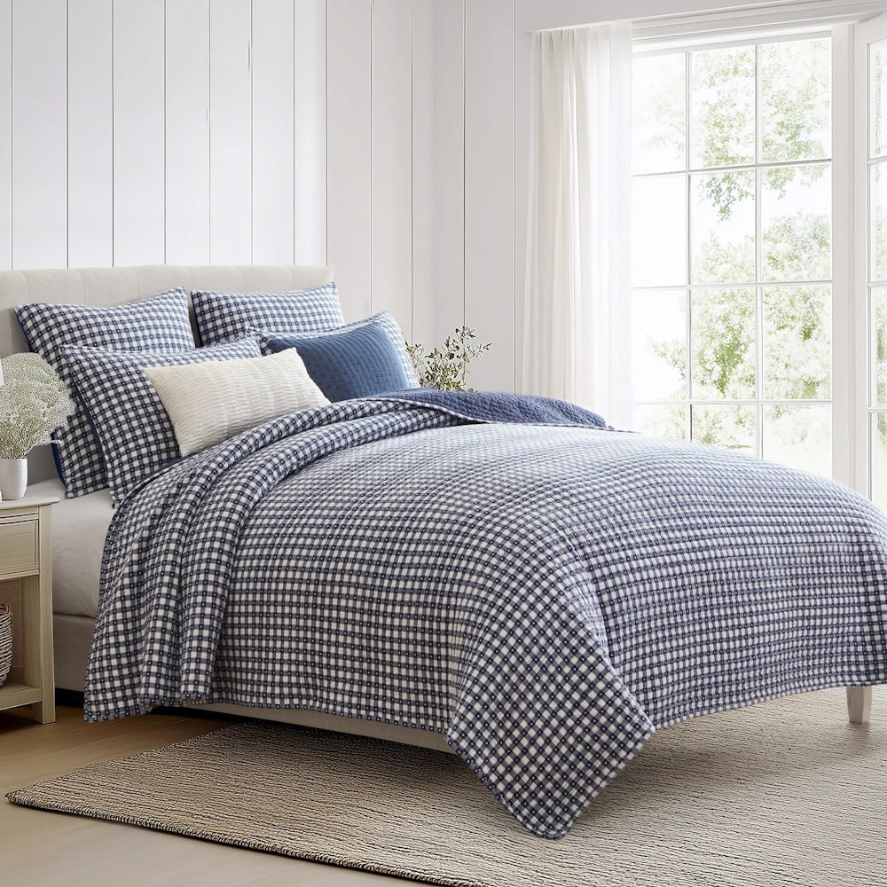 Bed styled with a navy blue and white gingham quilt set, matching shams, and accent pillows.