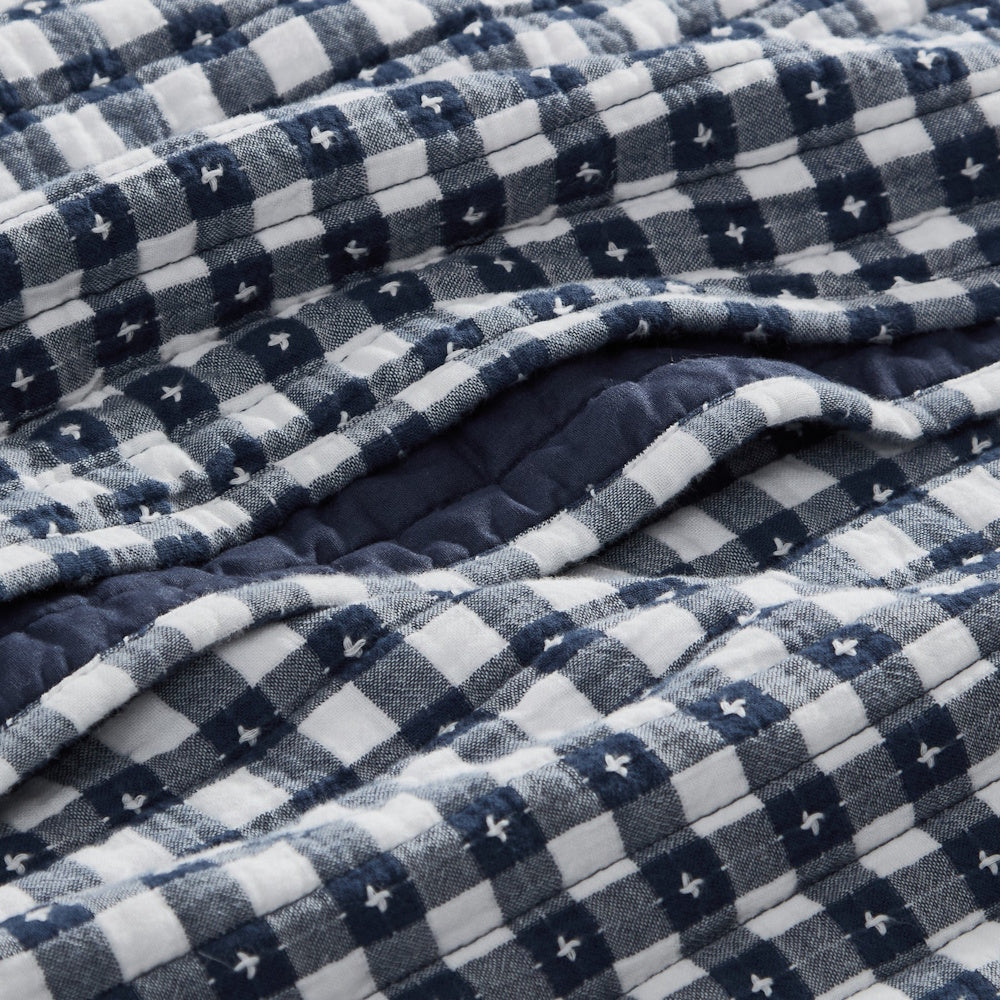 Close-up of a blue and white gingham quilted fabric featuring embroidered pick-stitch details.