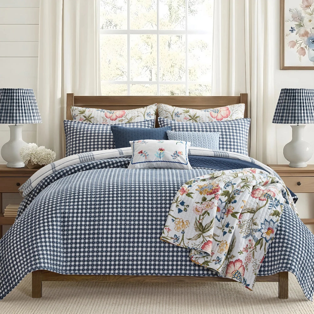 Navy and white gingham quilt set on a wooden bed, accented with a floral throw quilt and matching pillows.