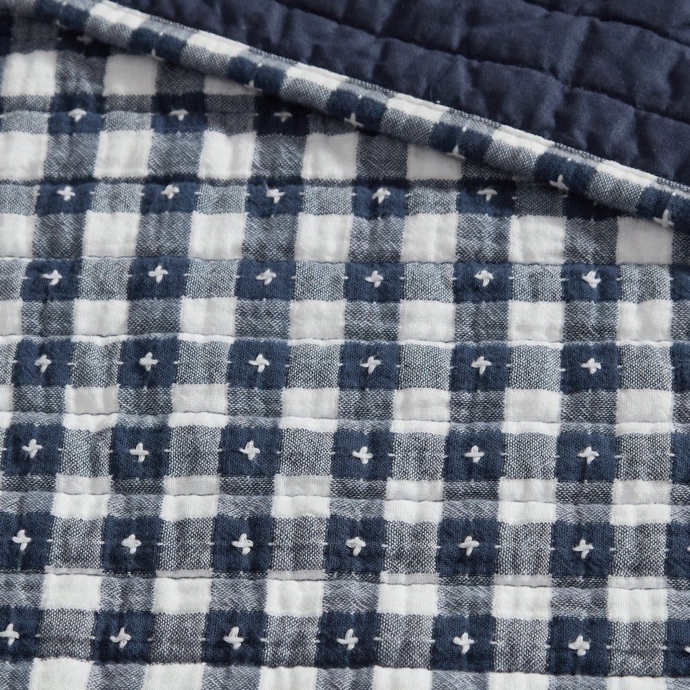 Close-up of a navy and white gingham quilt with white cross-stitch details and a solid navy back.