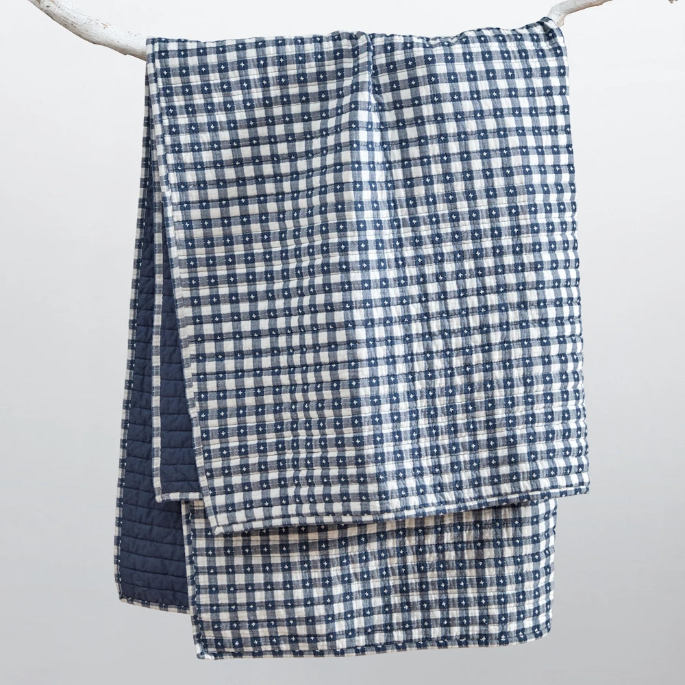 Navy blue and white gingham quilted throw blanket hanging on a branch with a solid navy reverse.