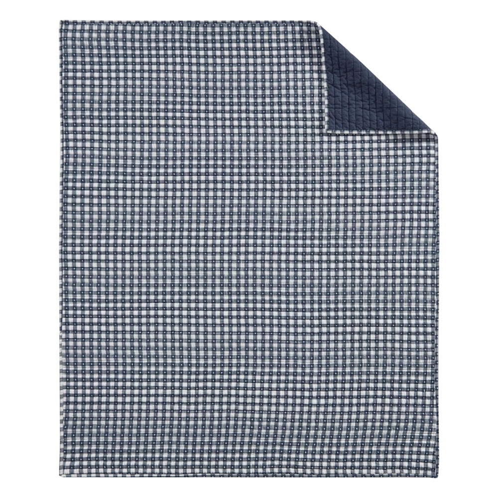 Navy blue and white gingham quilted throw blanket with top corner folded back to show solid navy backing.