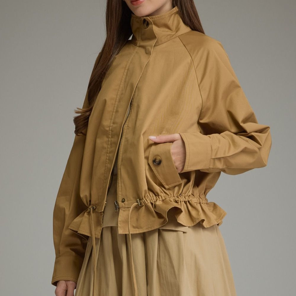 Three-quarter view of a camel full-zip jacket featuring a ruffled drawstring hem and pocket detail.