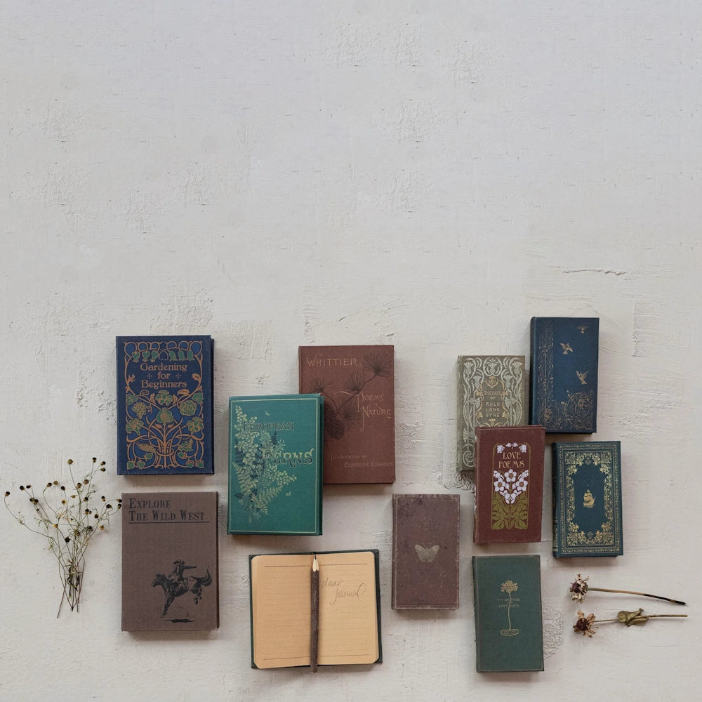 Vintage-style nature and poetry notebooks arranged on a textured wall with a small open journal and dried flowers.