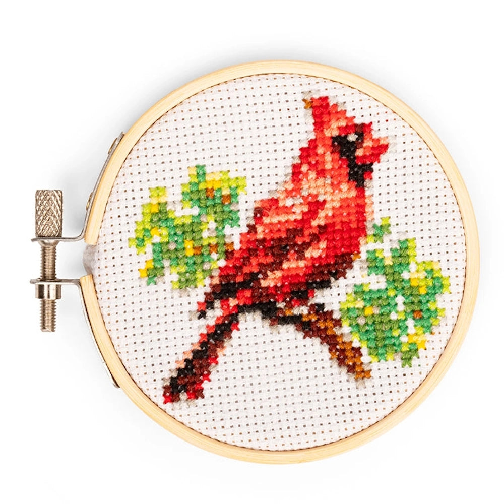 Mini cardinal cross-stitch kit featuring a red bird on a green branch in a wooden embroidery hoop.