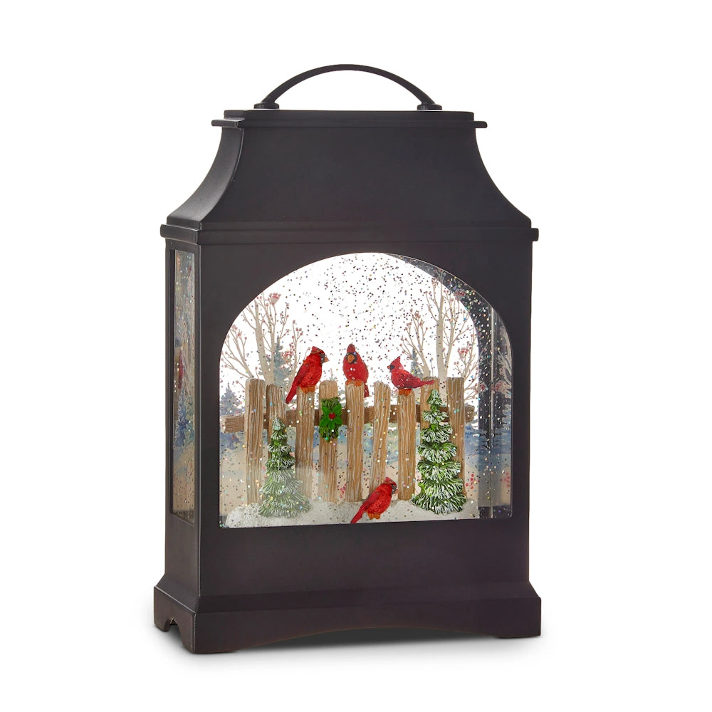 A black lighted water lantern featuring winter cardinals on a wooden fence with snow and trees.