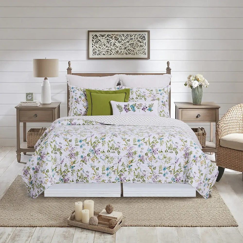 A bed with a floral quilt and green accent pillows, flanked by wooden nightstands in a bright, rustic room.