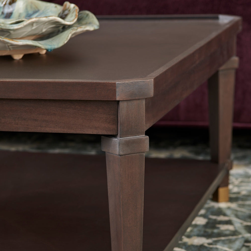 Close-up of a dark brown wooden coffee table with a rectangular top and tapered legs featuring gold-toned accents.