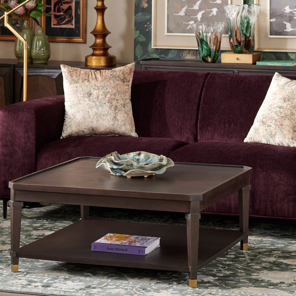 Modern dark wood coffee table with a lower shelf in a living room featuring a plum velvet sofa and floral pillows.