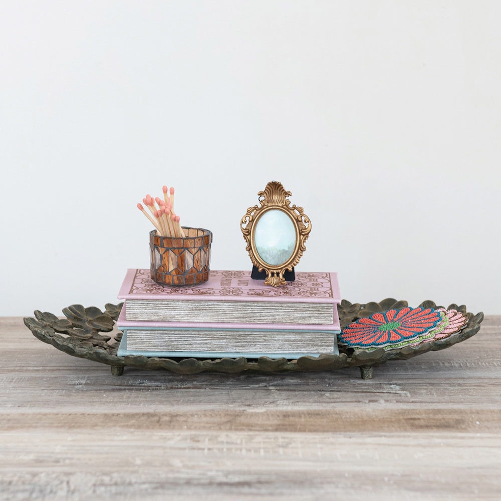 Cast aluminum flower tray holding decorative books, matches, a vintage gold frame, and colorful coasters.