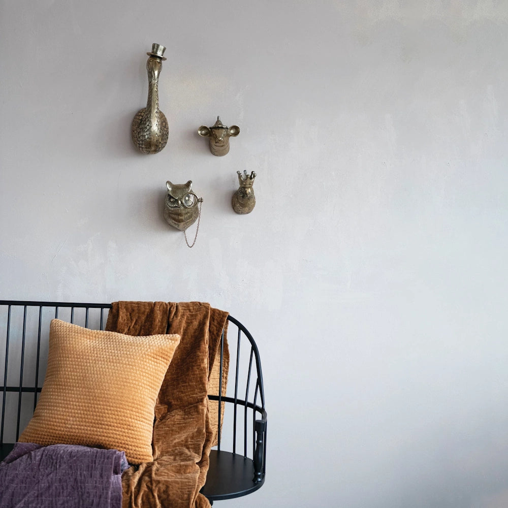 Cast aluminum animal head wall decor featuring a mouse, owl, and swan above a black bench with gold and purple pillows.
