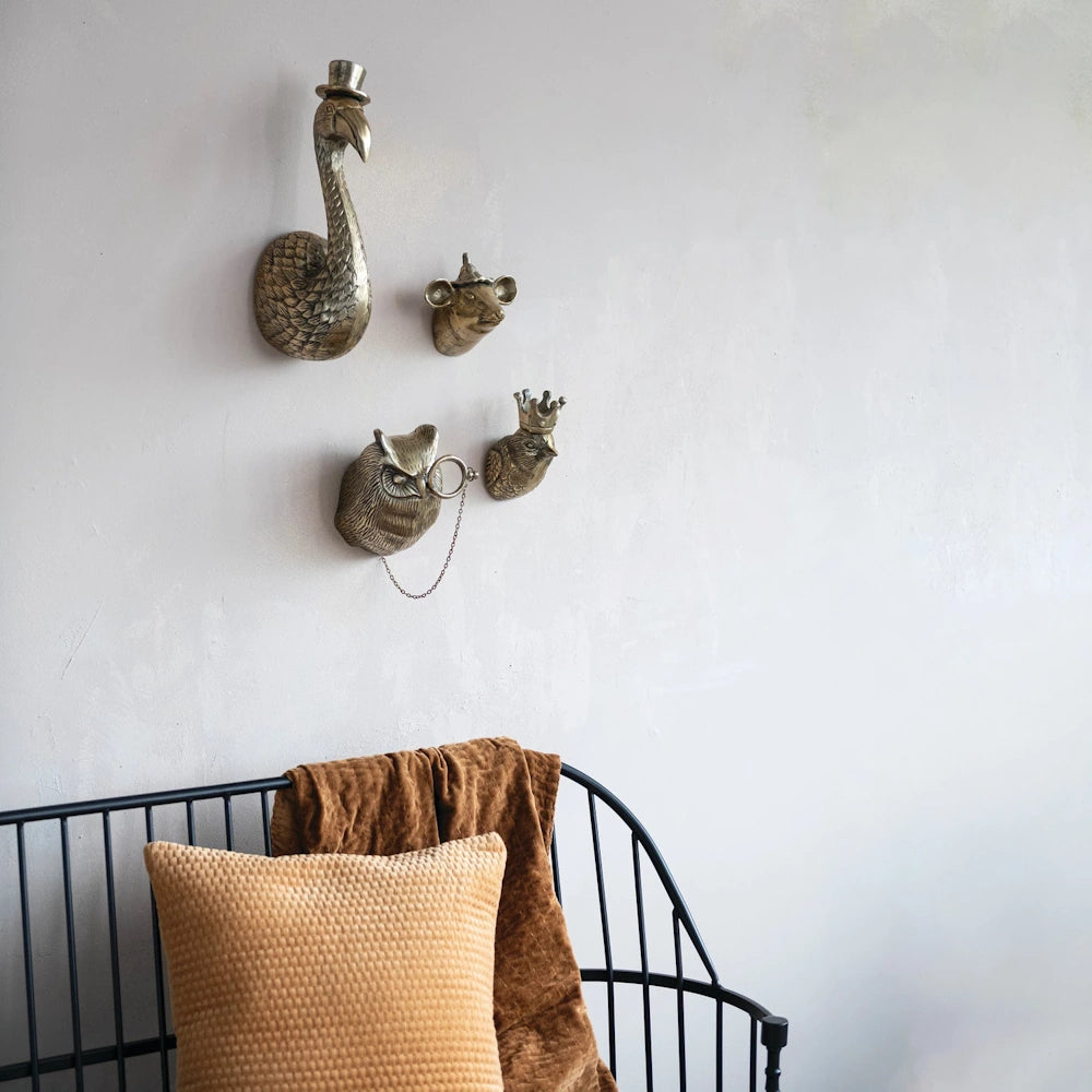 Cast aluminum gold animal head wall decor featuring a flamingo, mouse, owl, and bird with crowns and hats above a black bench.