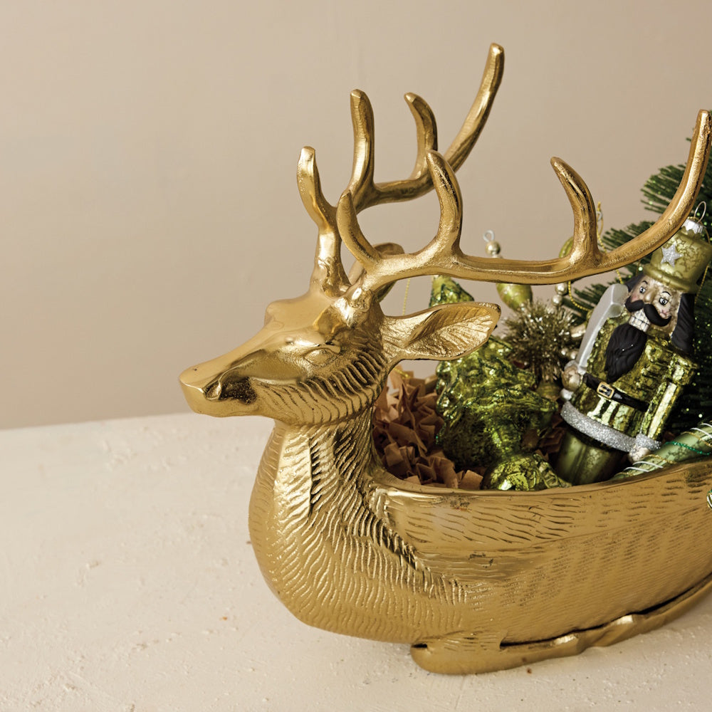 A gold cast aluminum reindeer-shaped bowl filled with a nutcracker and green ornaments.