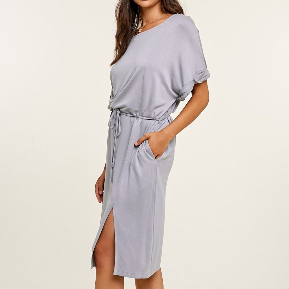 Side view of a woman wearing a grey t-shirt midi dress with a drawstring waist and a front thigh slit.