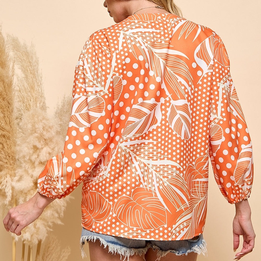 Back view of a woman wearing a long-sleeved orange blouse with a white polka dot and tropical leaf print.