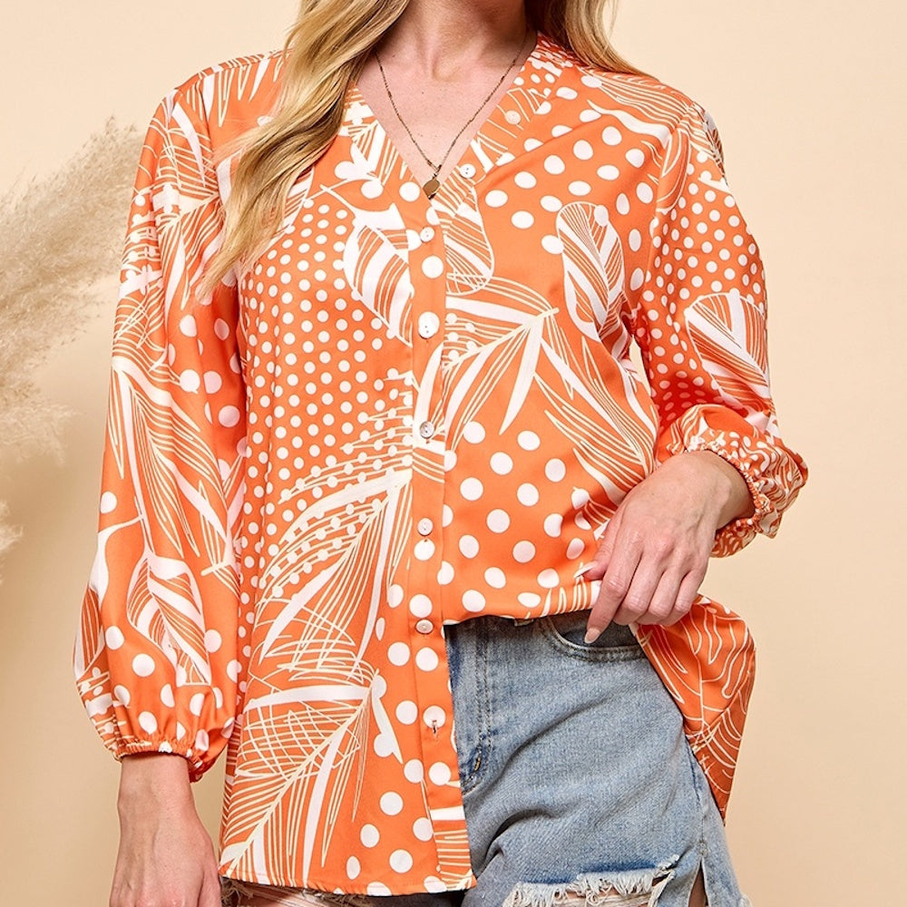 Orange and white long-sleeve button-up blouse with polka dot and tropical leaf prints, worn with denim shorts.