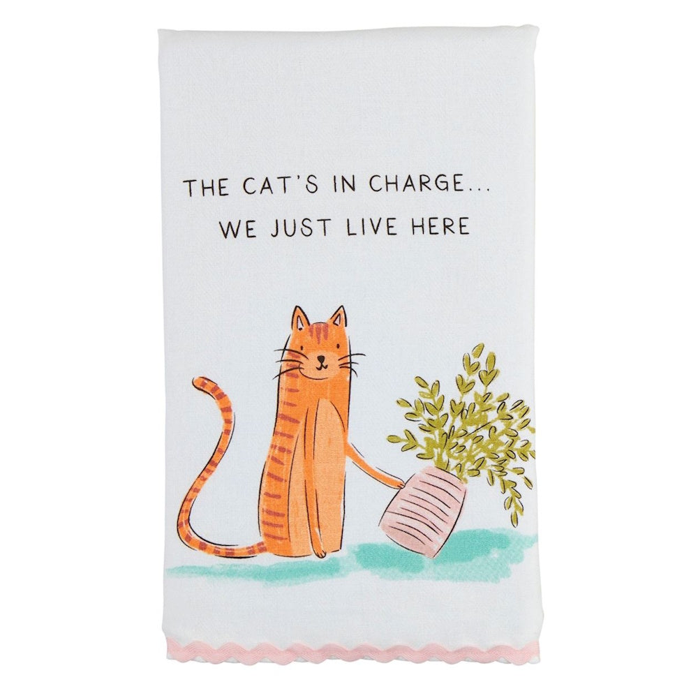 White towel with an orange tabby knocking over a plant and text: "THE CAT'S IN CHARGE... WE JUST LIVE HERE".