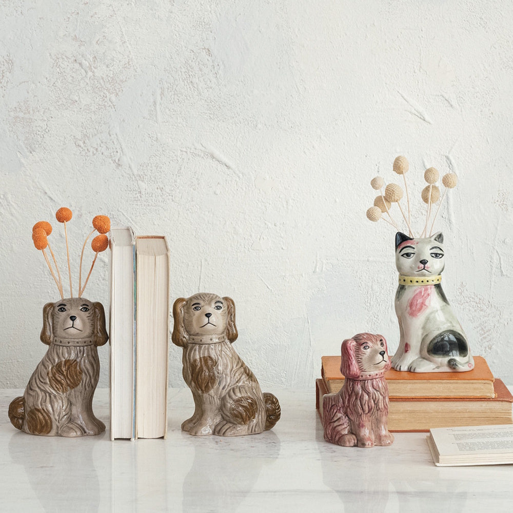 Four ceramic animal figurines, including two dog bookends and a cat vase with dried flowers, on a marble surface.