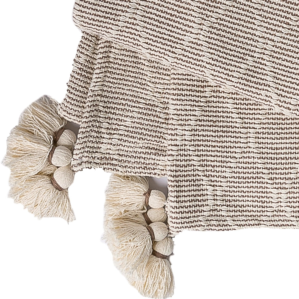 Close-up of a woven neutral blanket or throw with large, decorative cream tassels.