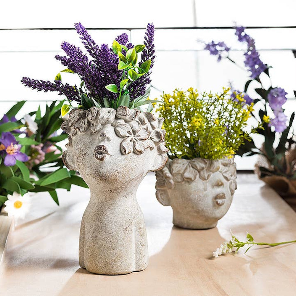 Two cement face planters with kissing lips, holding purple lavender and yellow flowers on a table.