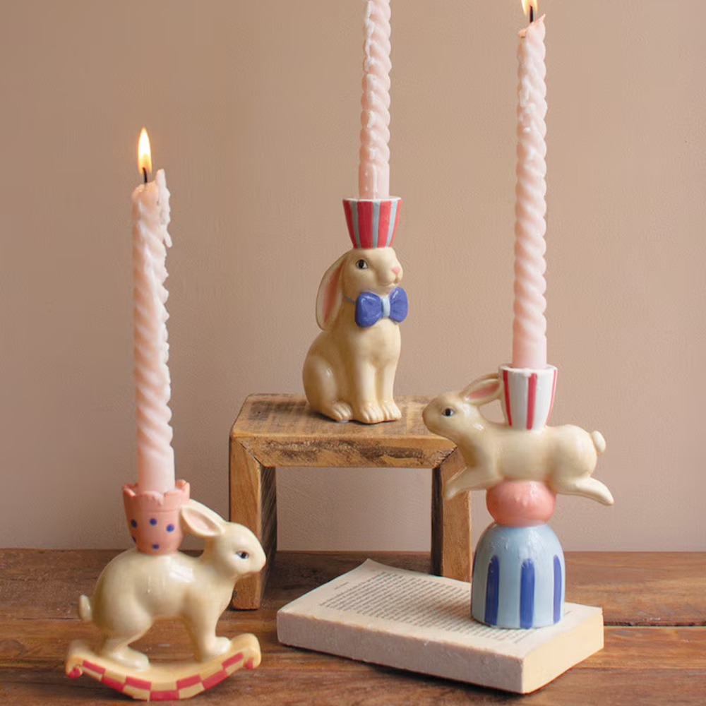 Whimsical ceramic bunny taper candle holders with spiral pink candles on a wooden table.