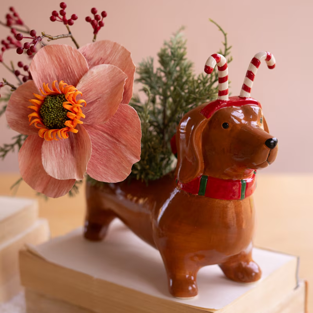 Close-up of ceramic dachshund planter wearing candy cane headband with floral arrangement.
