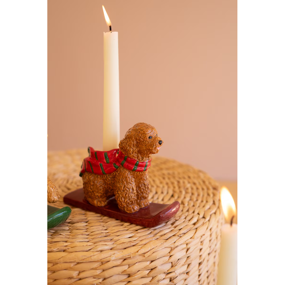 Close-up of a curly brown poodle taper candleholder wearing a green and red scarf on a brown sled.