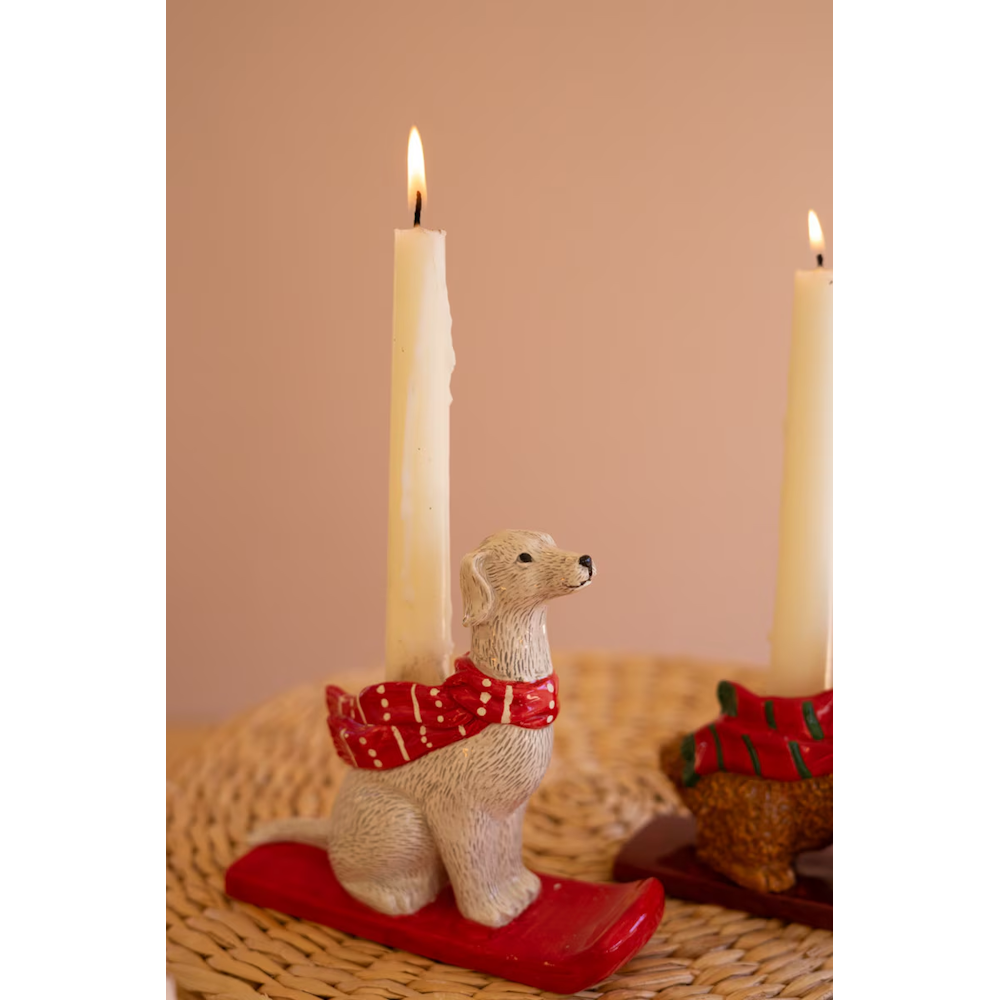 Close-up of a white dog taper candleholder wearing a red polka dot scarf on a red sled.