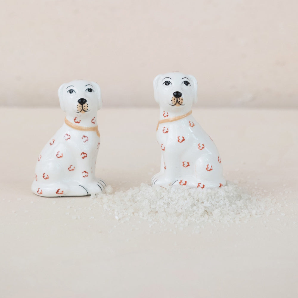 Ceramic dog-shaped salt and pepper shakers sitting next to a pile of salt on a neutral beige background.