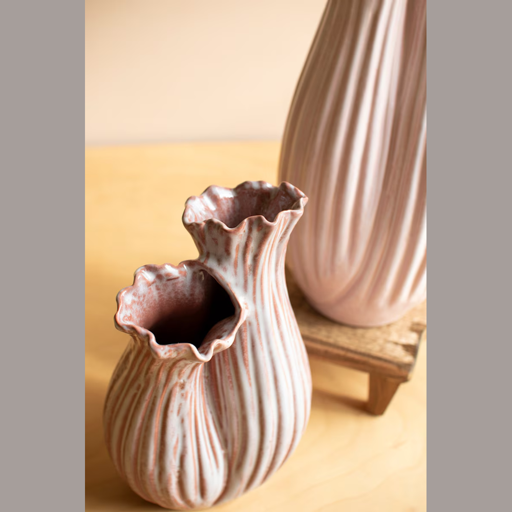 Organic fluted ceramic bud vase with a double-neck design in a textured pink and white glaze on a wooden table.