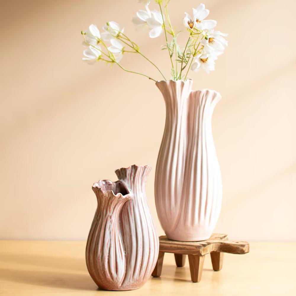 Two fluted ceramic vases in soft pink and white with an organic, wavy texture and white flowers in the taller vase.