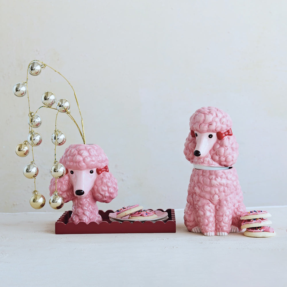 Pink ceramic poodle vase holding metallic ornament branches, alongside a matching poodle jar.