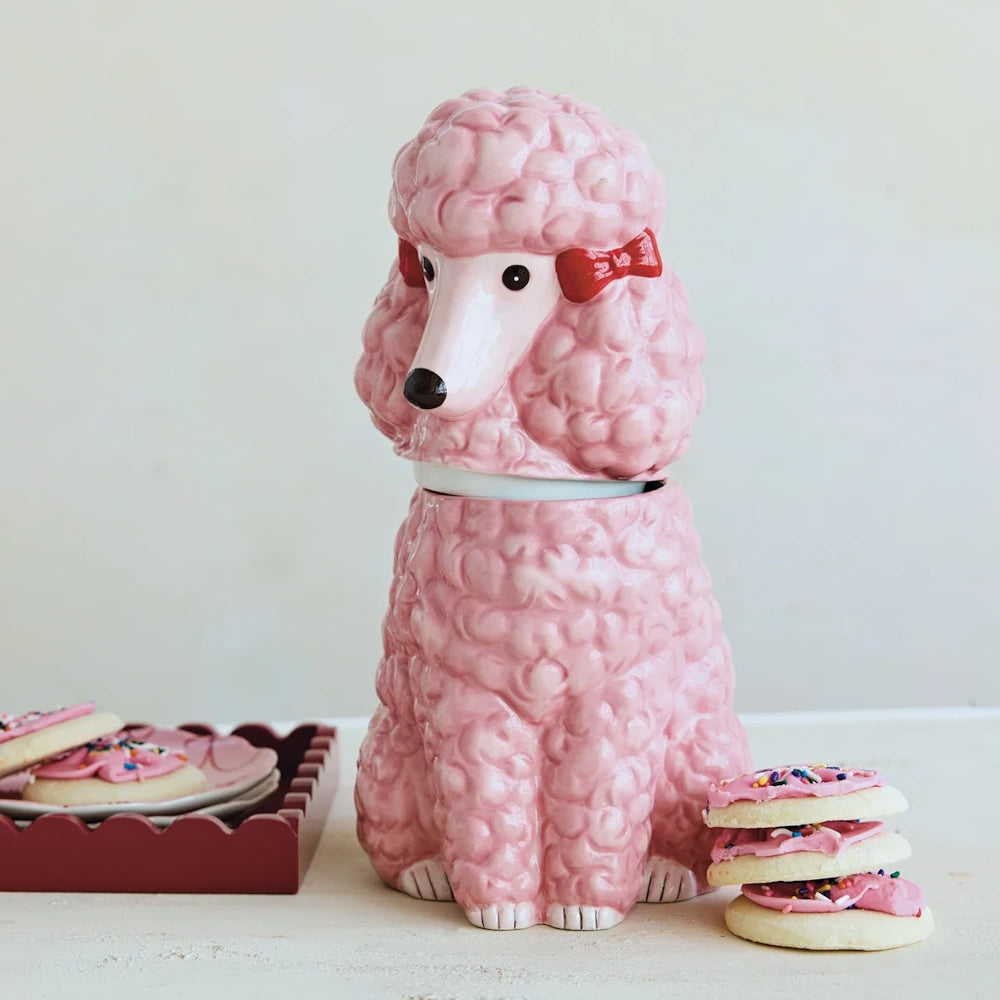 Pink ceramic poodle cookie jar with red bows, displayed with frosted cookies on a counter.
