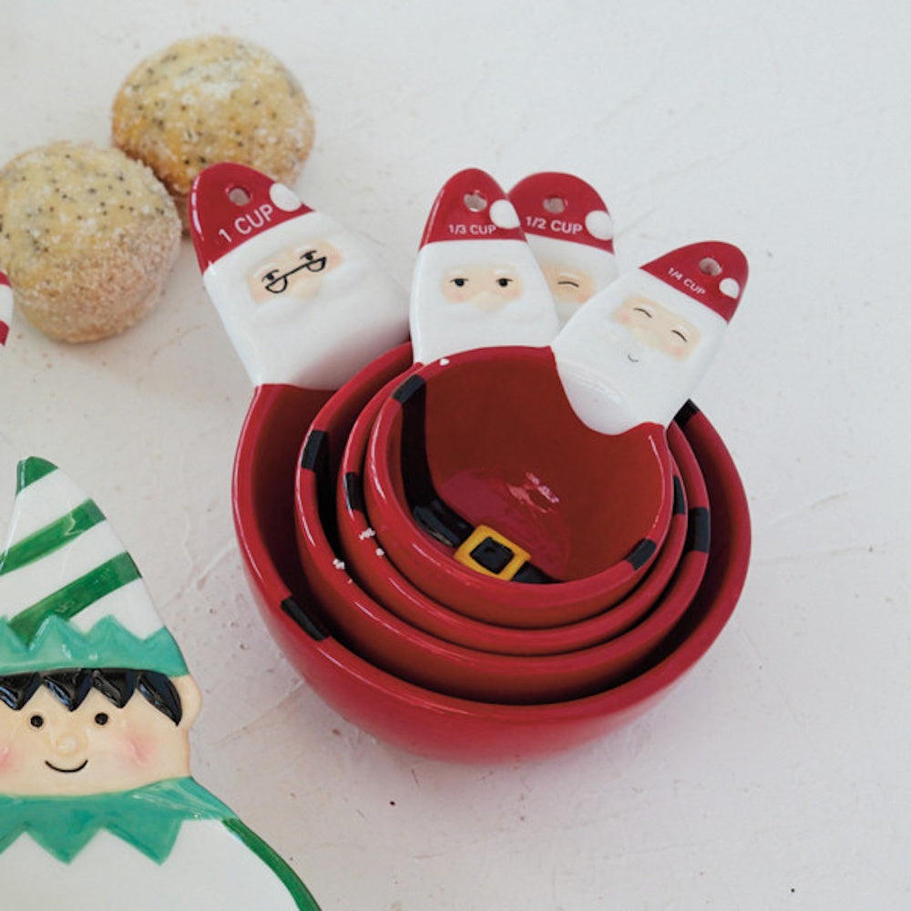 Nested Santa Claus ceramic measuring cups alongside small baked treats and an elf-themed item.