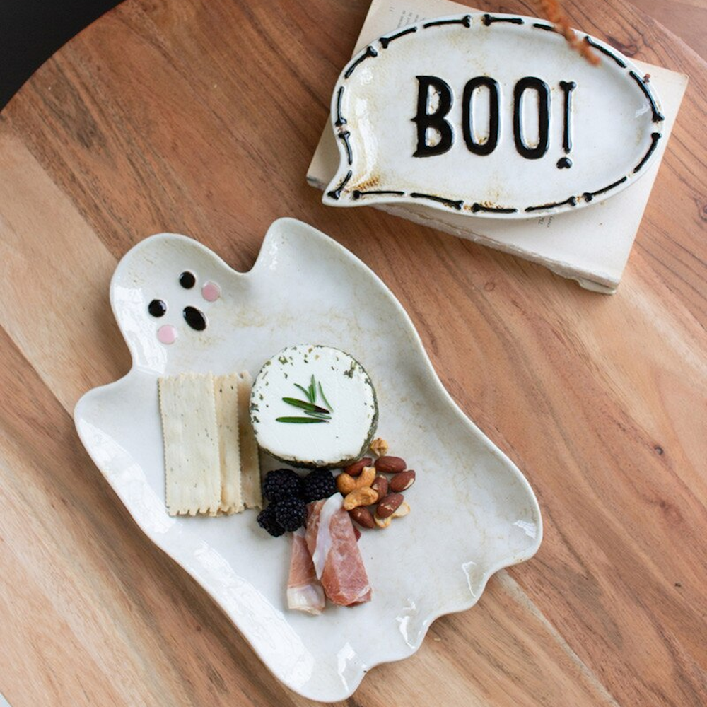 Ghost and BOO ceramic serving platters with snacks on a wooden table, Halloween party food ideas.