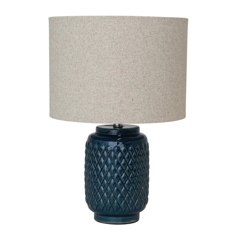 Blue textured ceramic table lamp with a diamond pattern base and a beige linen drum shade on a white background.