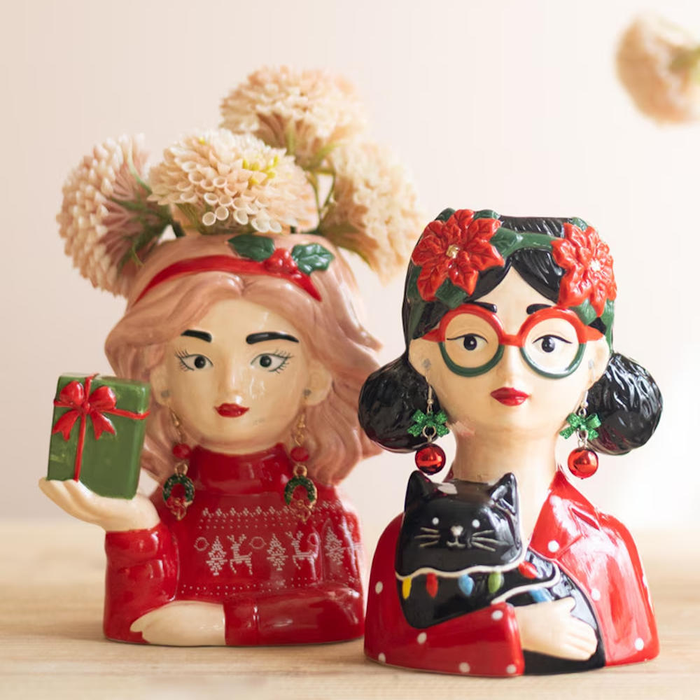 Close-up view of festive holiday woman head vases holding a wrapped gift and a black cat.