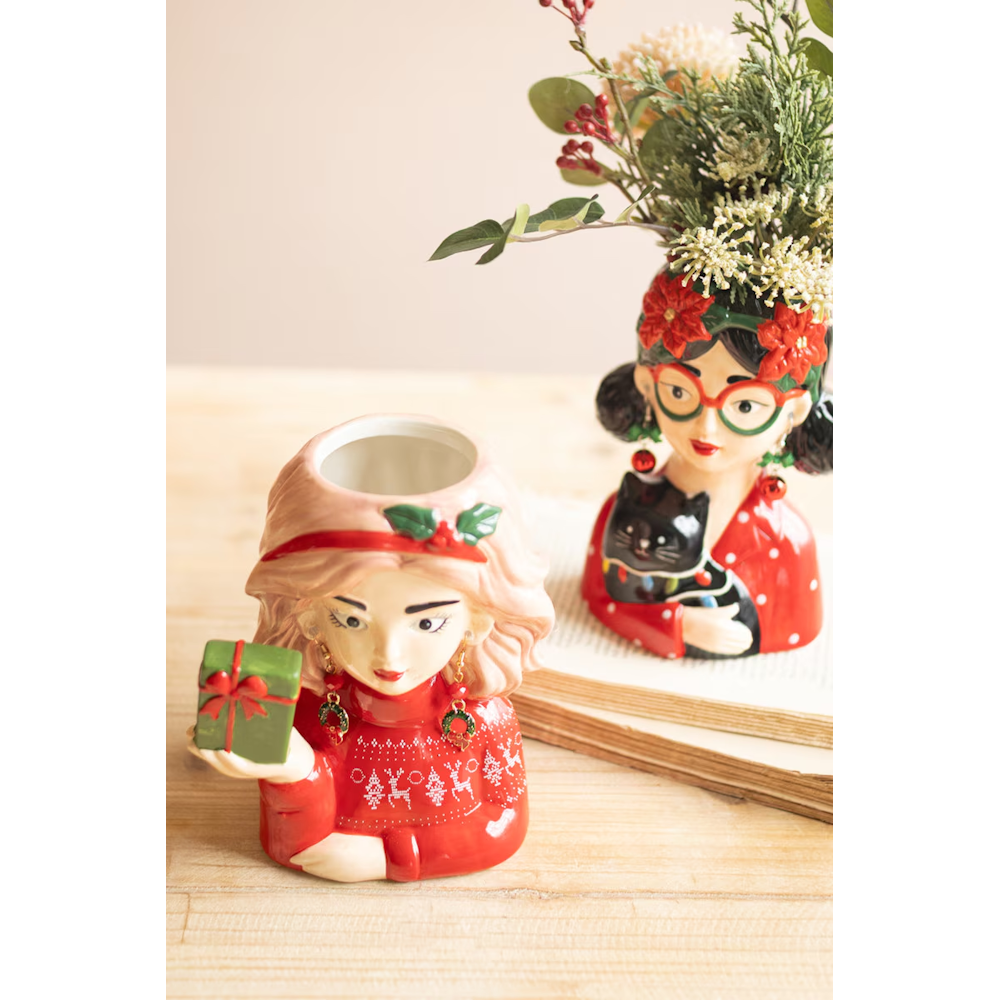 Two ceramic lady head Christmas vases arranged on a table with a holiday floral arrangement.