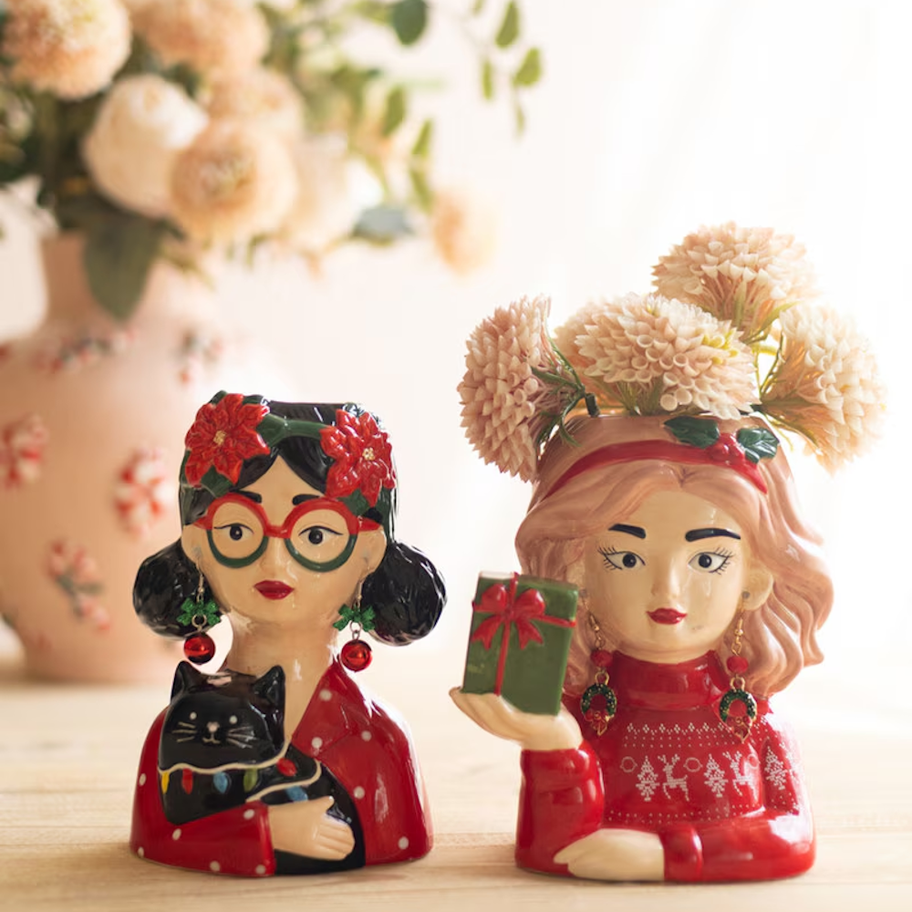 Two whimsical ceramic lady head vases styled with festive holiday sweaters, accessories, and flowers.