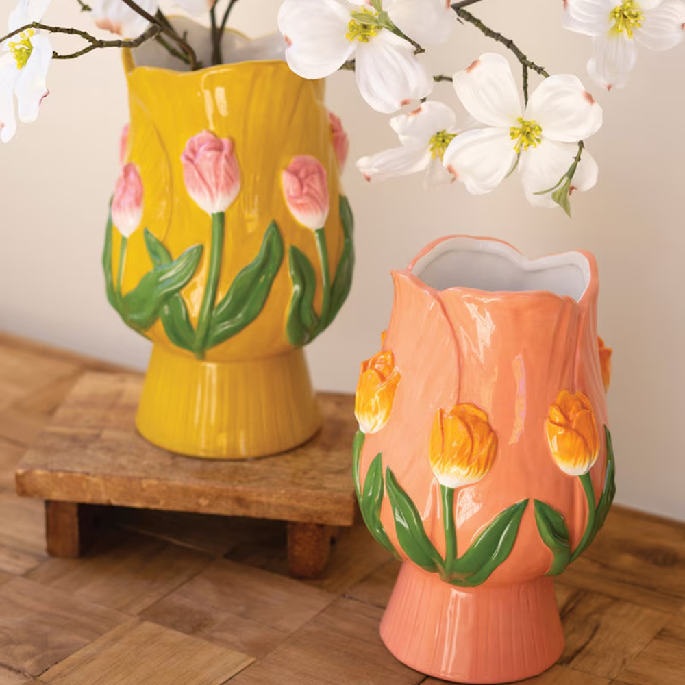 Yellow and peach ceramic tulip-shaped vases with embossed floral details on a wooden table with white blossoms.