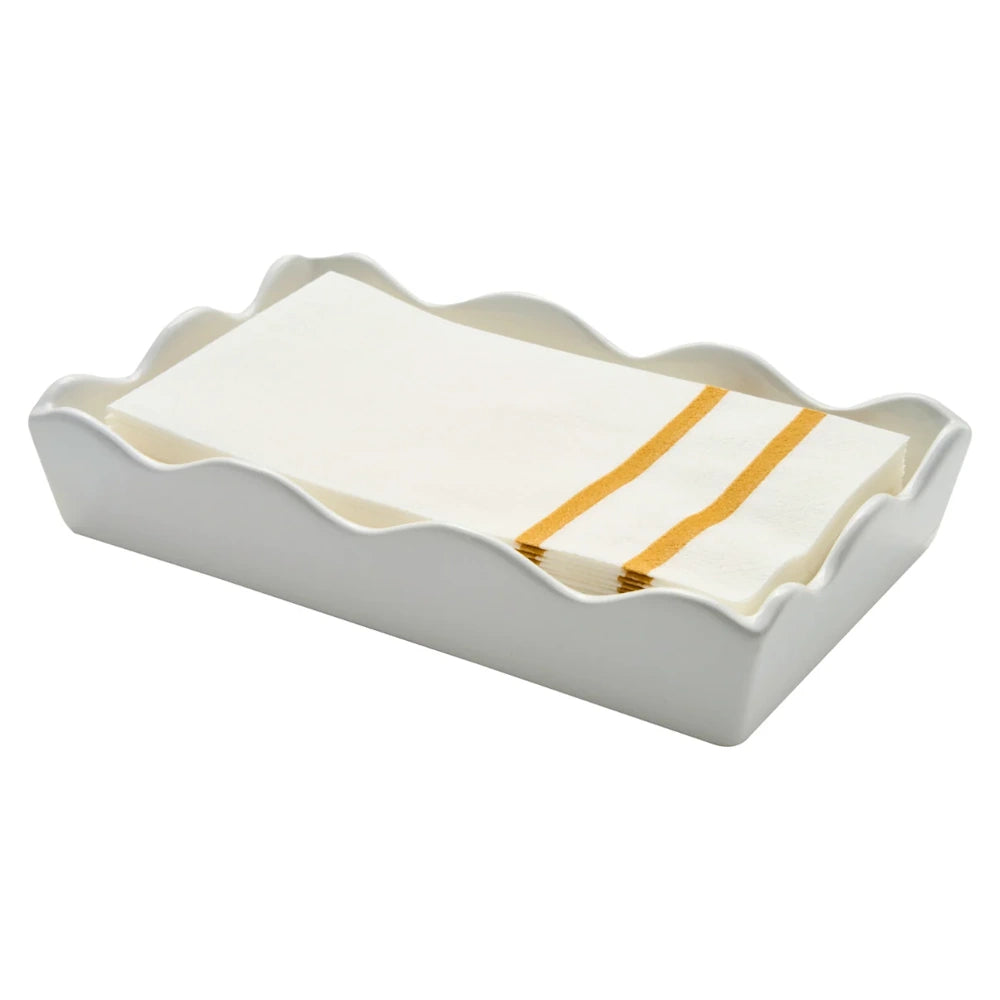 Side angle view of a white ceramic wave guest towel tray holding folded paper napkins with gold stripes.