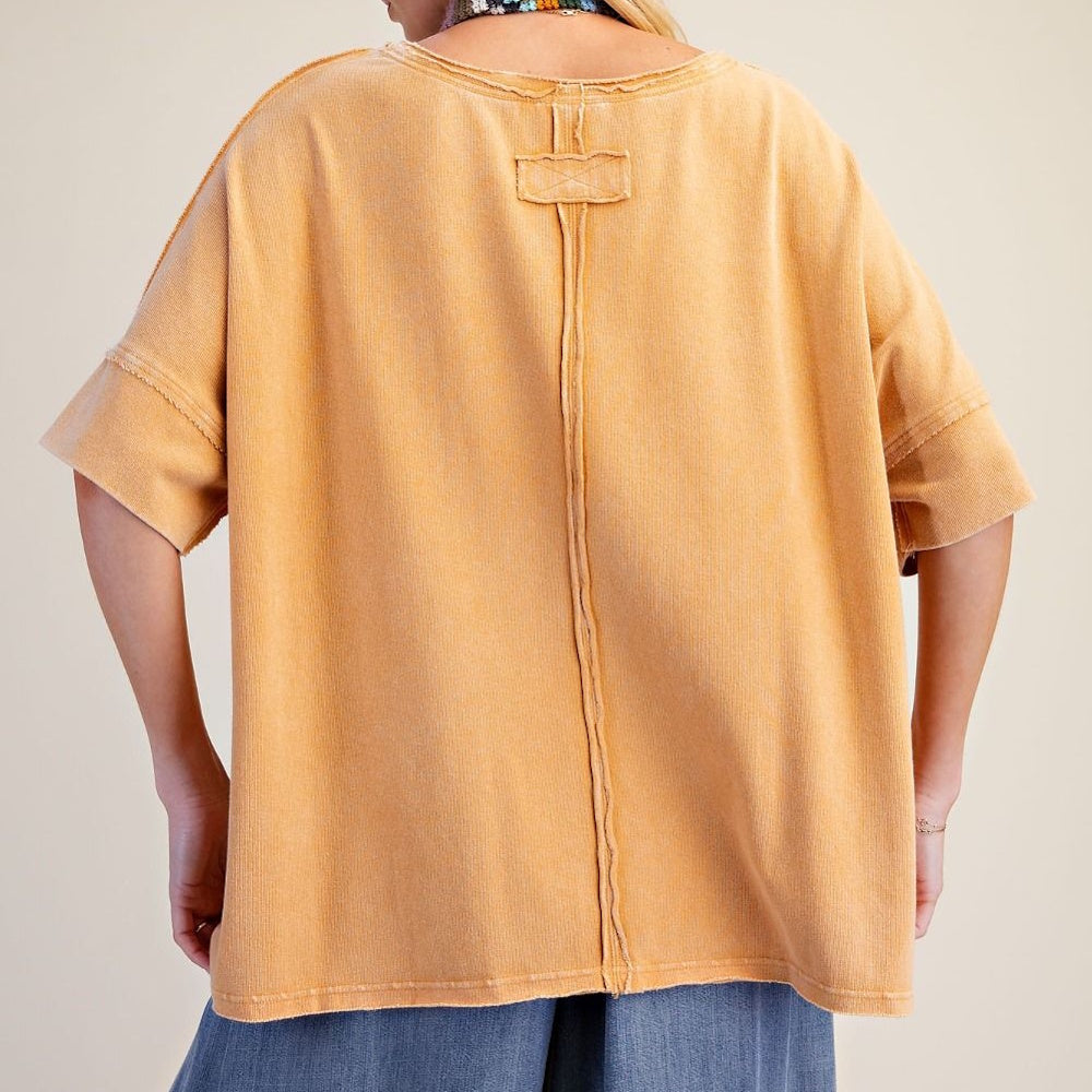 Back view of a person wearing a loose, mustard-yellow short-sleeve top with exposed central seam detailing.