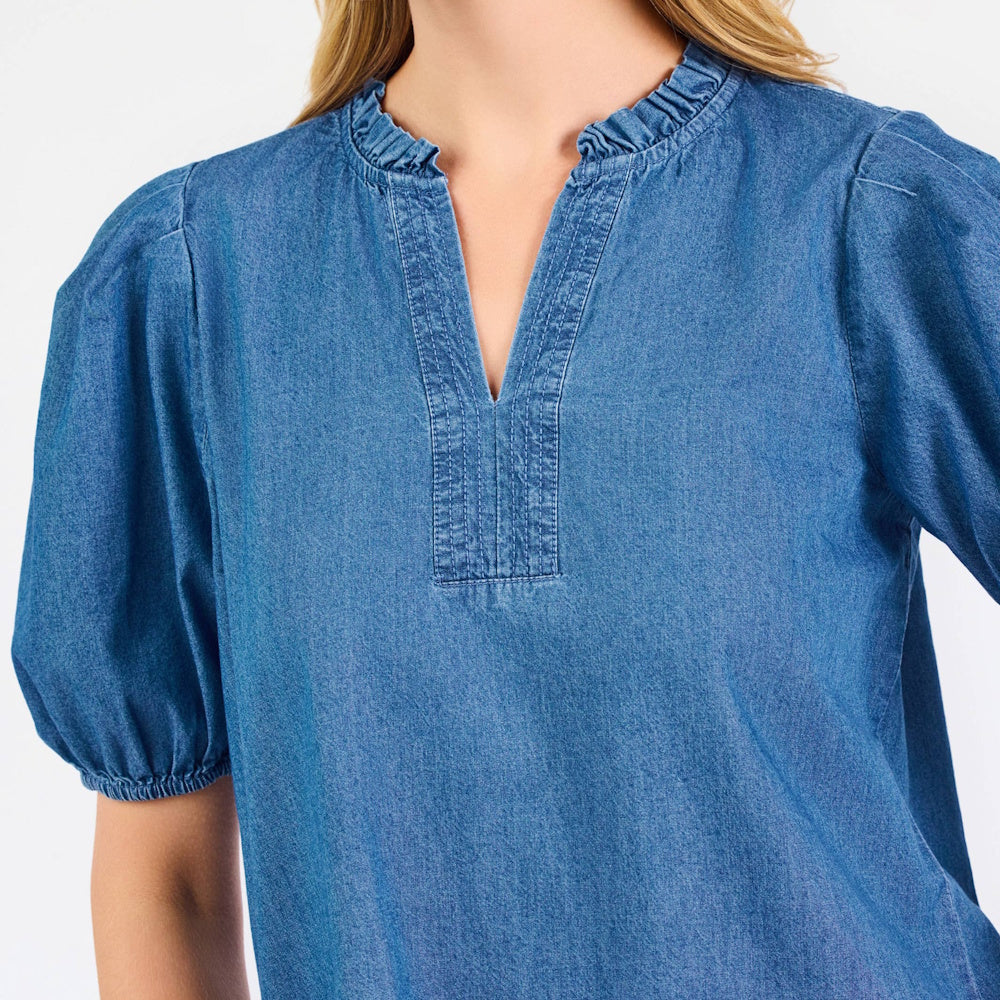 Woman wearing a blue chambray top with a ruffled V-neckline and puff short sleeves.