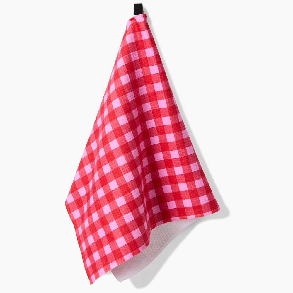 A red and pink gingham pattern hand towel hanging from a black hook against a white background.