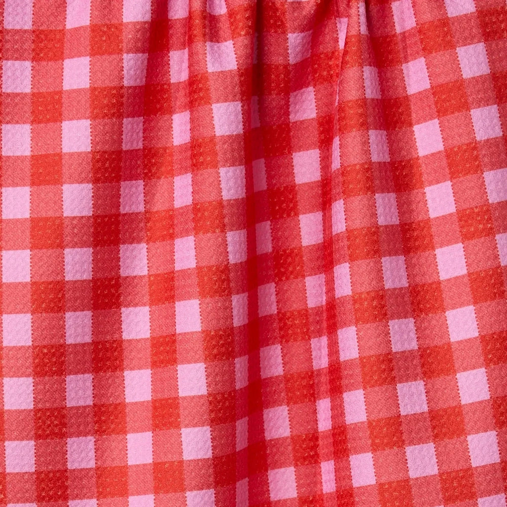A close-up of a textured fabric featuring a vibrant red and pink gingham checkered pattern with soft folds.